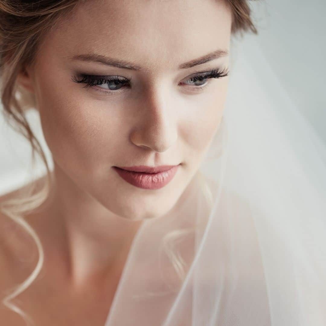 A bride and two bridesmaids seated together during treatment prep in a Bella Reina Spa treatment room, instrument trays and makeup palettes arranged along the counter