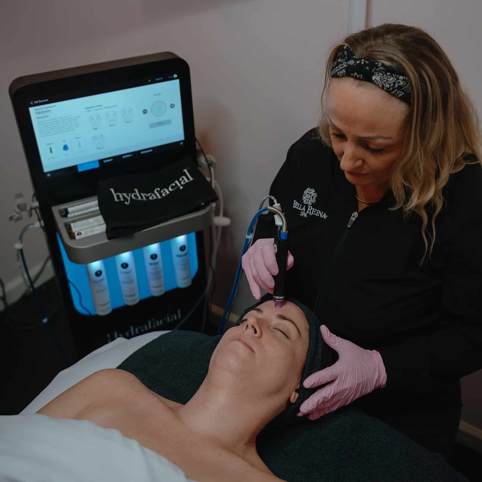 A Bella Reina esthetician performing a HydraFacial on the branded Syndeo system