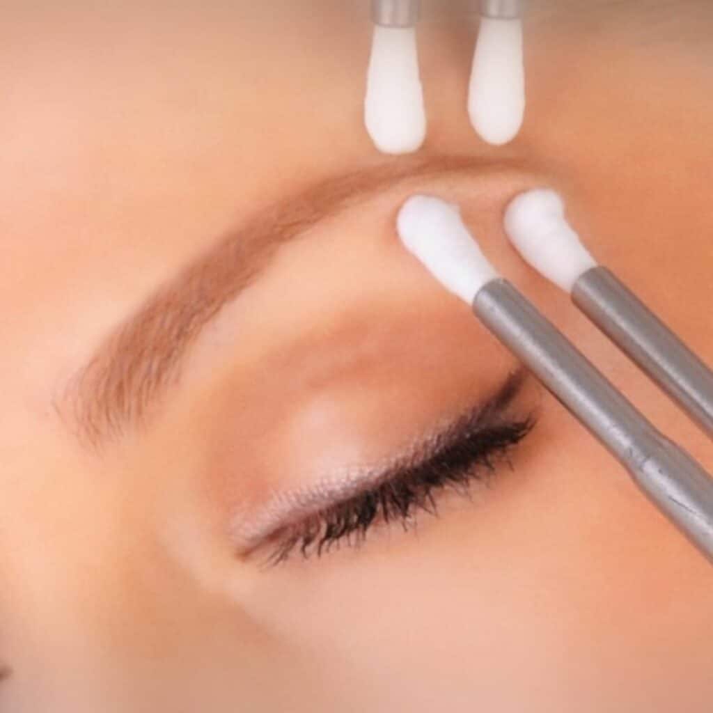 A microcurrent facial device with twin metal probes gliding along a client's jawline at Bella Reina Spa, practitioner's other hand steadying the client's chin under soft treatment-room light