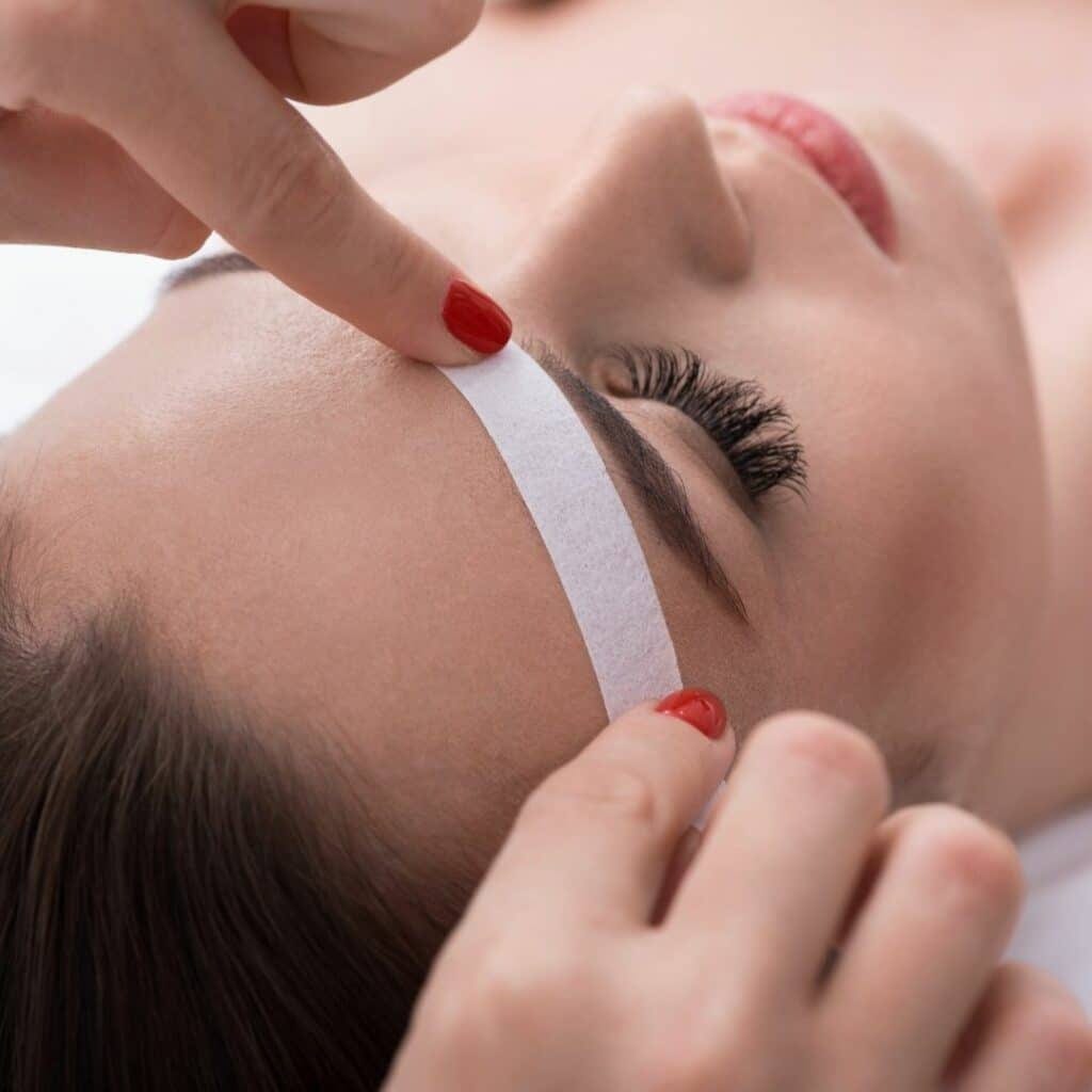 European hard wax and soft wax pots arranged on a stainless instrument tray in a Bella Reina Spa treatment room, muslin strips folded beside a warming pot